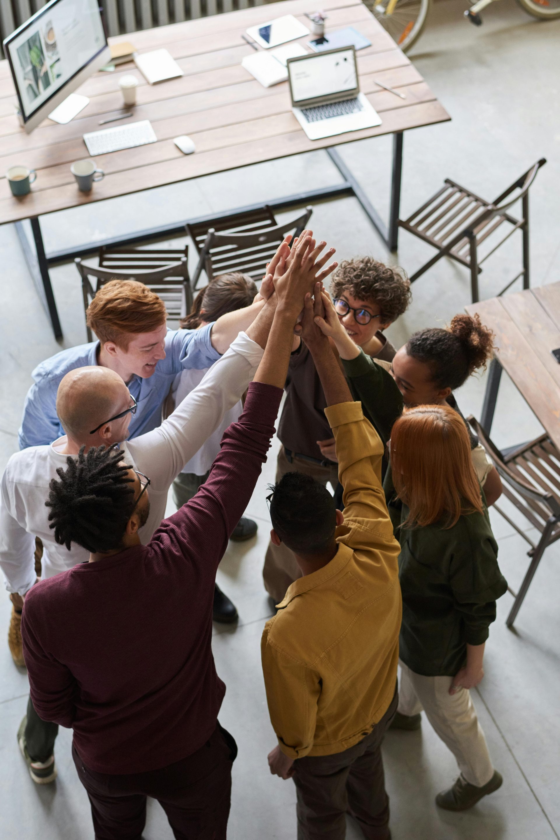 Eine Gruppe von Fachleuten aus verschiedenen Bereichen legt die Hände übereinander auf einen Tisch, um Teamwork und Zusammenarbeit zu symbolisieren.