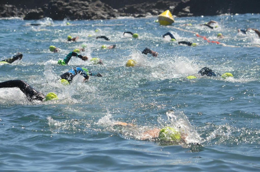 Wettkampfschwimmer bei einem Triathlon-Schwimmwettbewerb, die mit Badekappen durch die Gewässer des Ozeans spritzen.