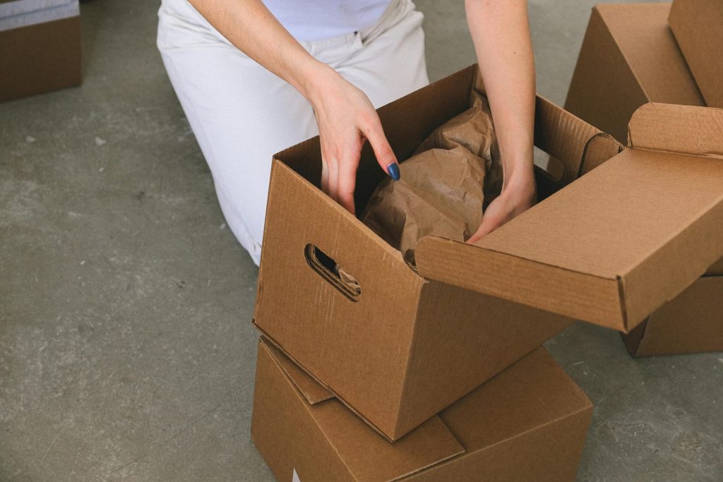 Von oben ist eine anonyme Frau zu sehen, die beim Umzug in ihre neue Wohnung verpackte Gegenstände in einen Karton packt.