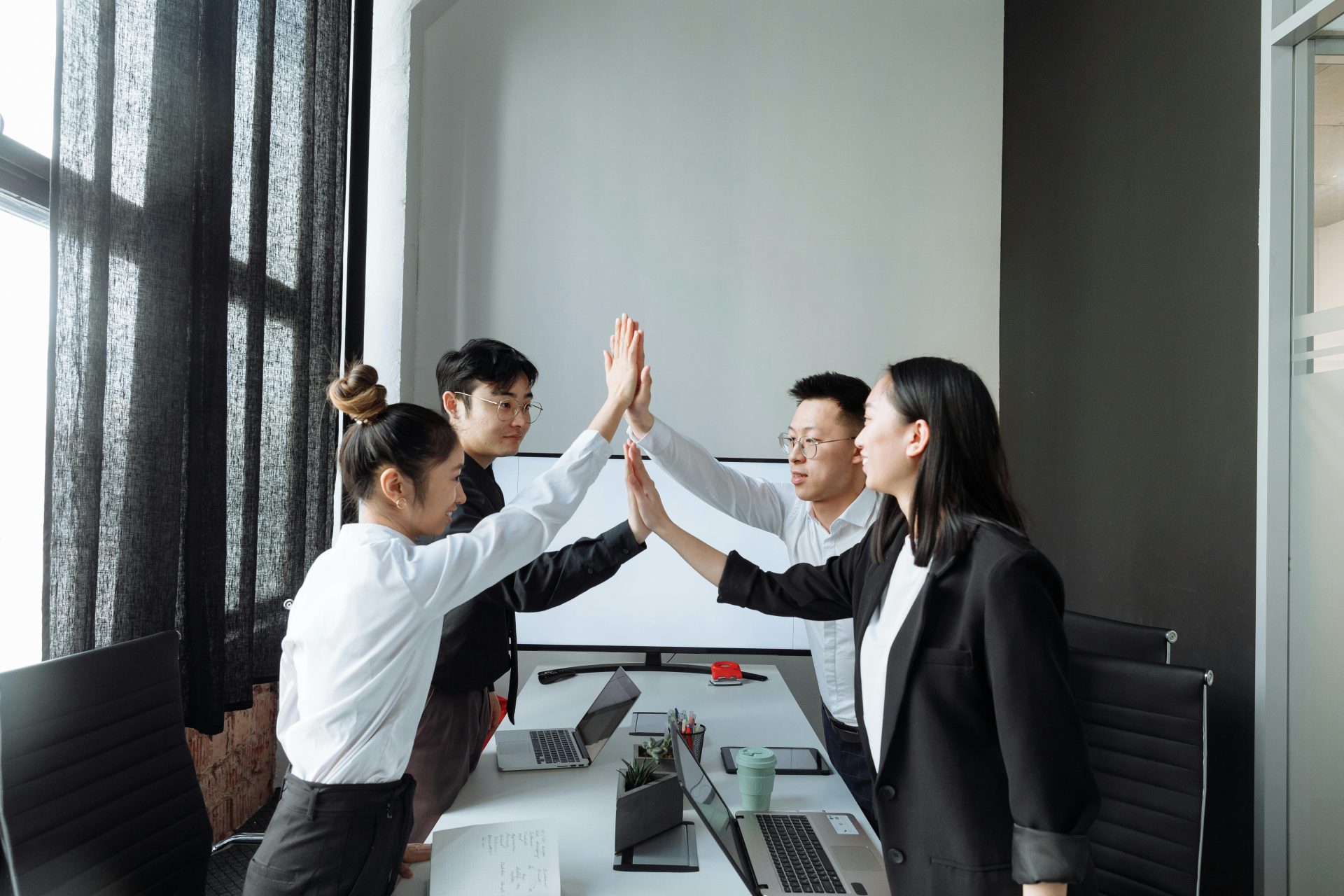 Vier Kollegen in einem modernen Büro geben sich ein High-Five und feiern damit Teamwork und Erfolg.