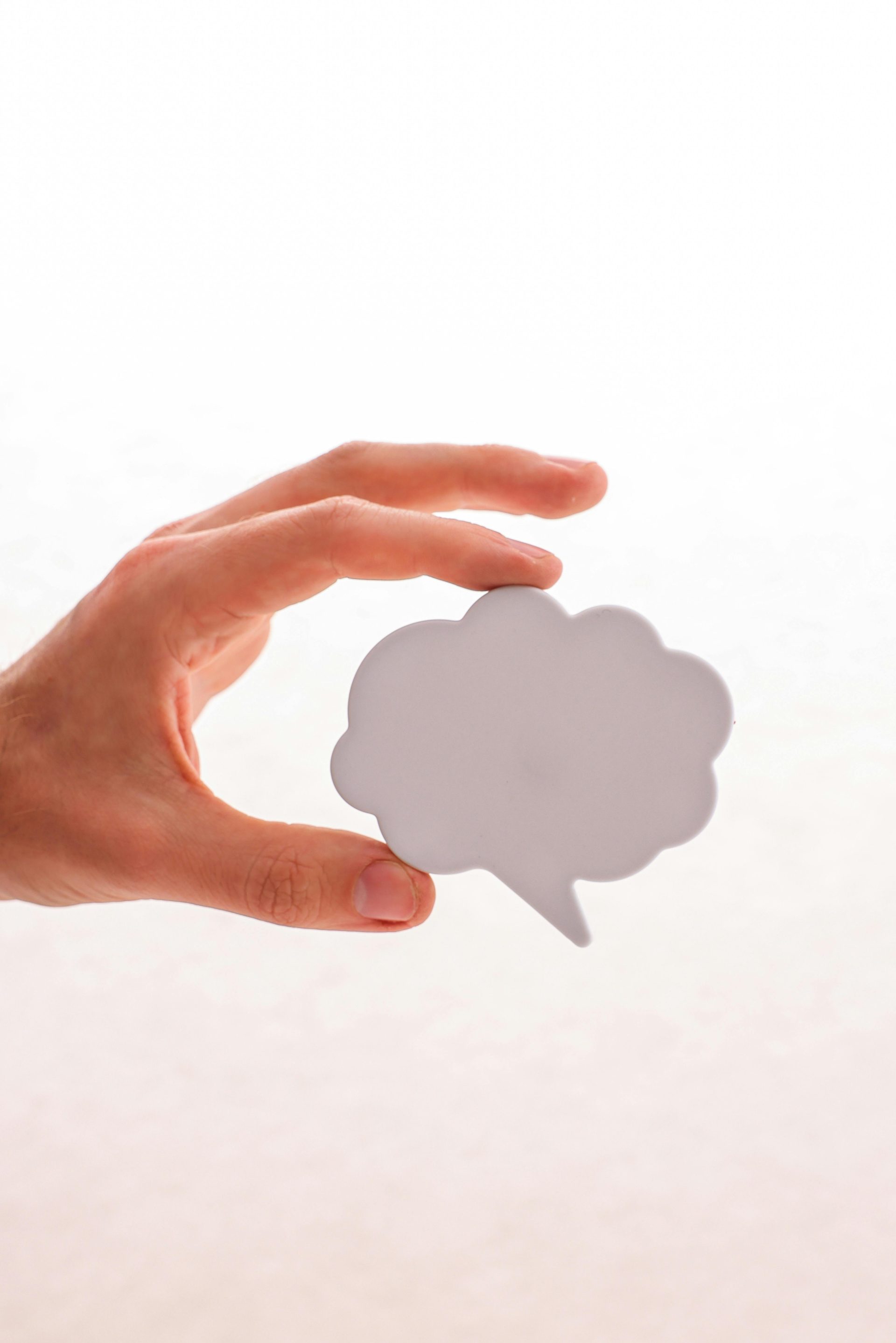 Eine Hand hält eine ausgeschnittene, wolkenförmige Sprechblase vor neutralem Hintergrund.
