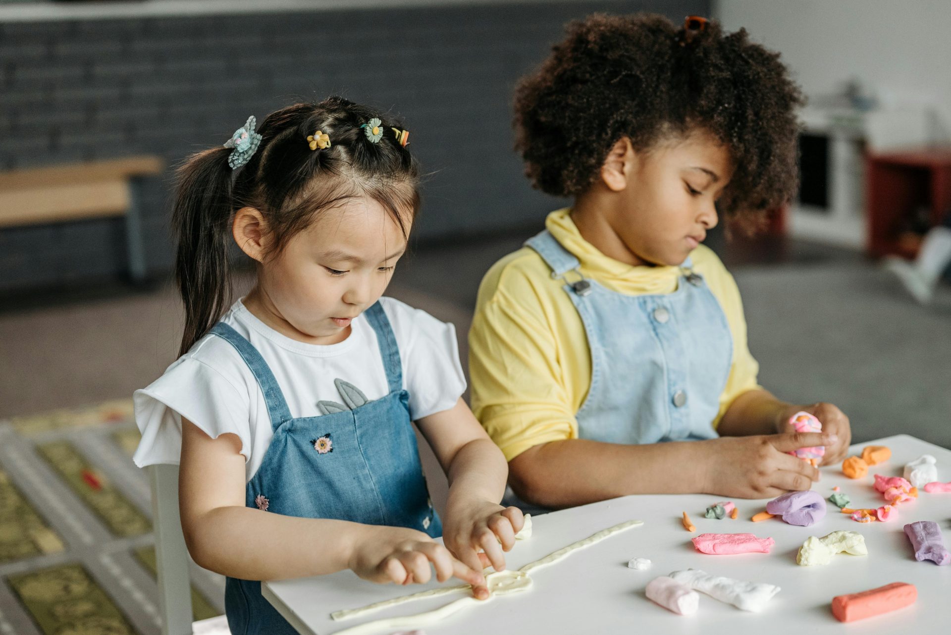 Zwei Kinder spielen drinnen mit buntem Ton und fördern dabei ihre Kreativität und Teamfähigkeit.